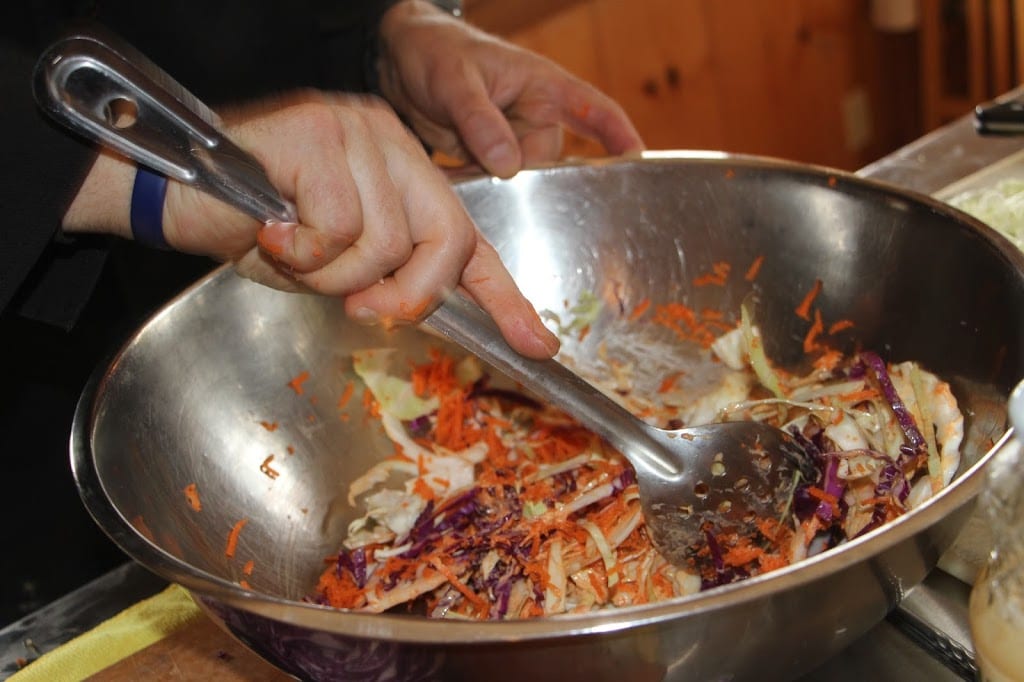Mixing tahini into the cabbage and carrots for the slaw