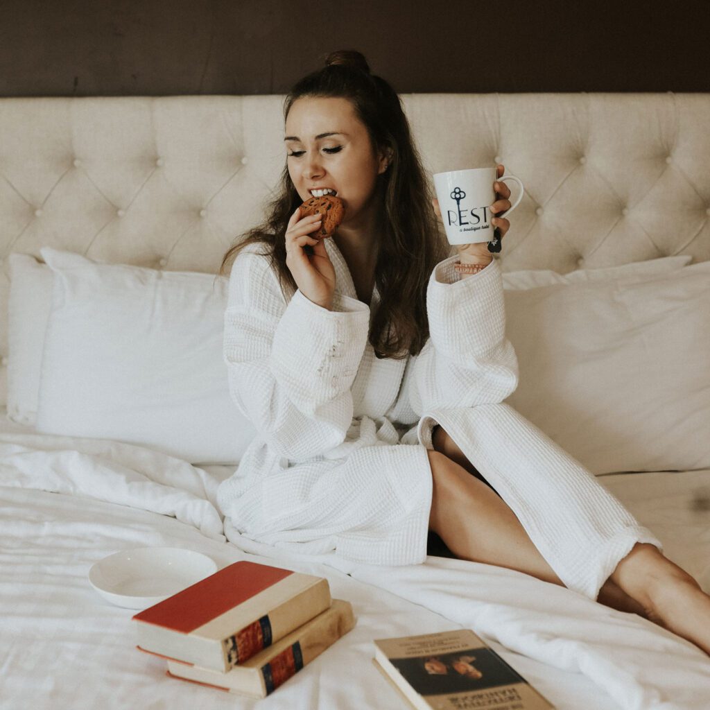 a woman in a robe enjoying cookies and coffee in bed at Rest, A Boutique Hotel