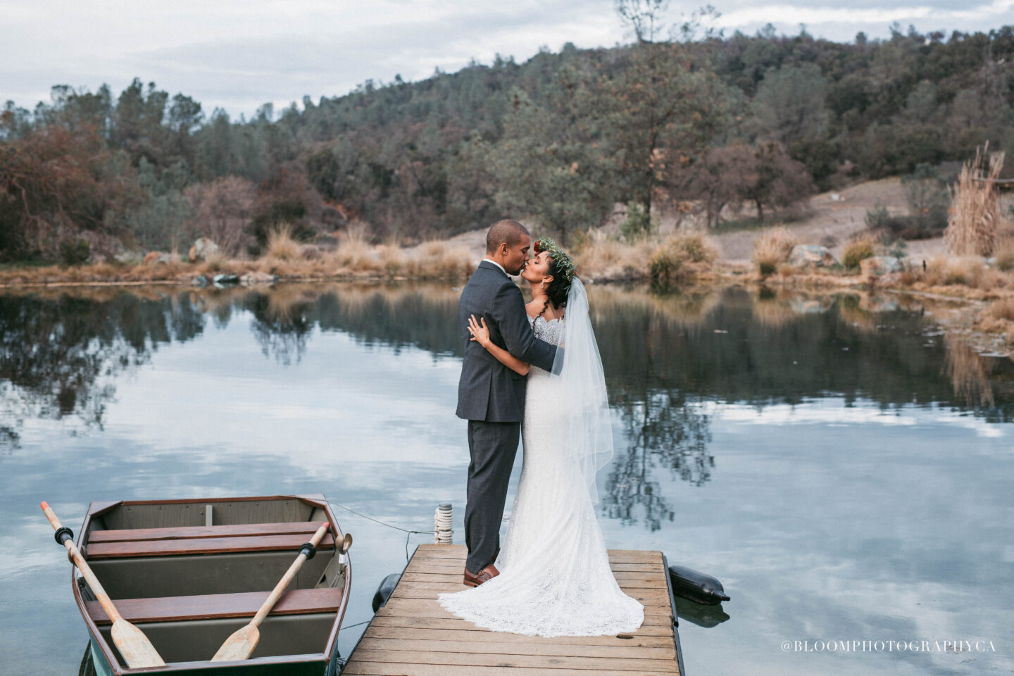 A bride and groom kissing on a wooden dock beside a pond amid rolling hills at Eden Vale Innn