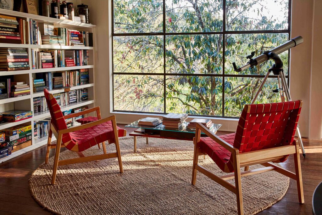 Living room with bookshelves and modern red chairs facing a picture window at Mine + Farm