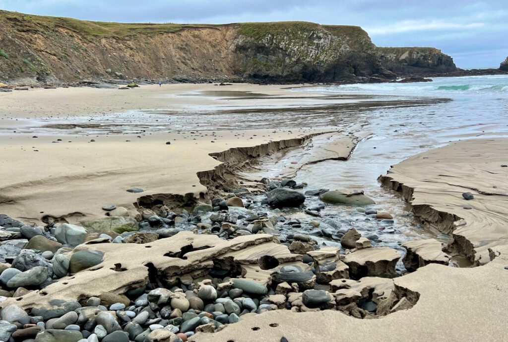 Rock-strewn stream running to the ocean at Cooks Beach with headlands in the background