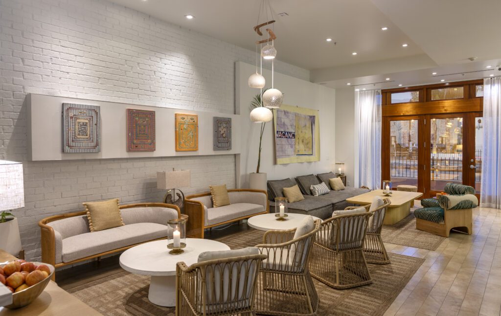 A modern lobby with sofas, chairs and coffee tables, a modern light fixture hangs from the ceiling and modern artwork displayed on the walls with large floor to ceiling wood framed glass doors and windows