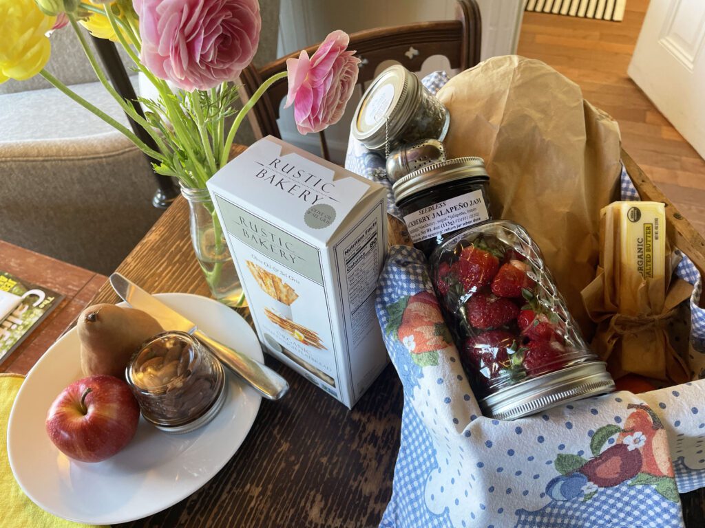 A basket filled with fresh fruit, crackers, bread, butter, and local jam.