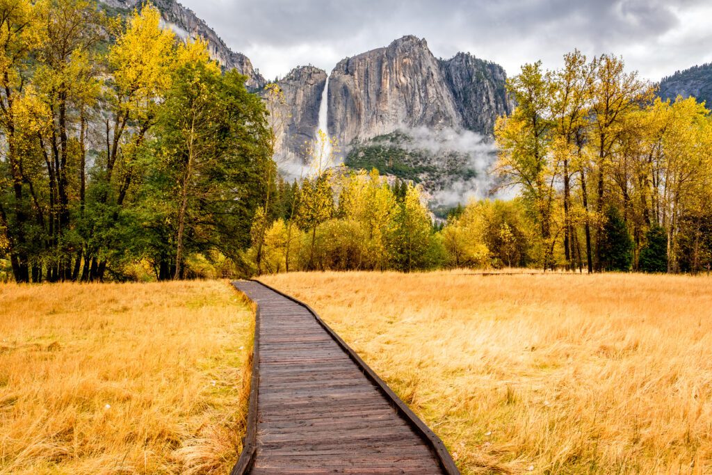 Meadow with boardwalk in Yosemite National Park Valley with Yosemite Falls at cloudy autumn morning. Low clouds lay in the valley. 