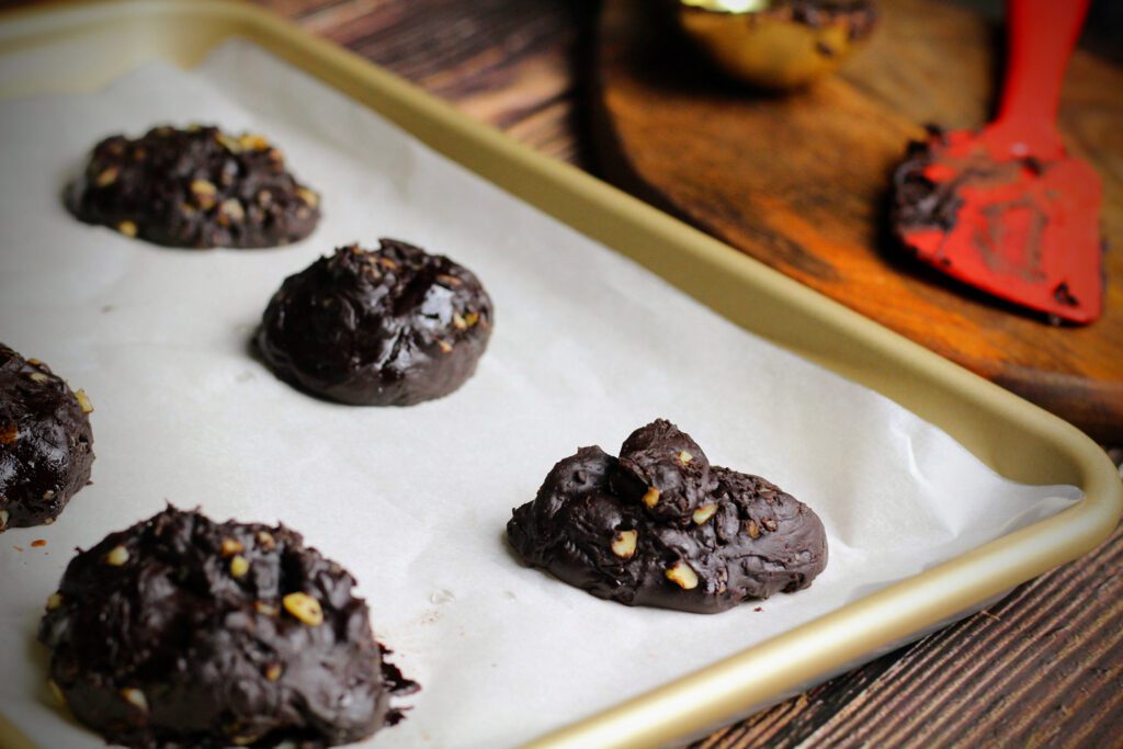 Transfer 1-ounce scoops of the chewy chocolate cookie dough onto greased parchment paper, then bake for 12 to 15 minutes at 350 degrees Fahrenheit.