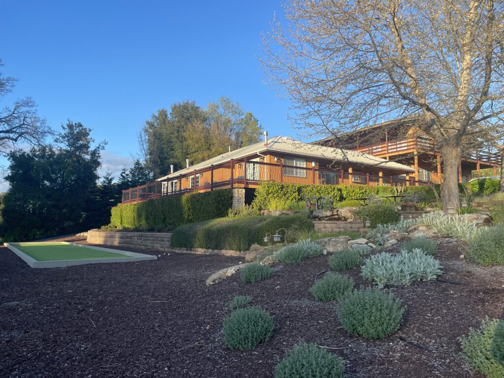 Exterior of The Inn at Opolo showing the wraparound veranda, bocce ball court, and terraced gardens.
