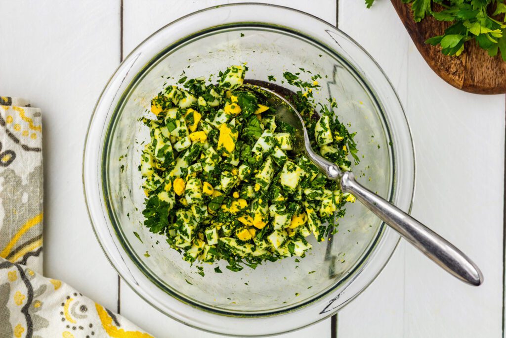 Mixing chopped hard-boiled eggs with fresh parsley.