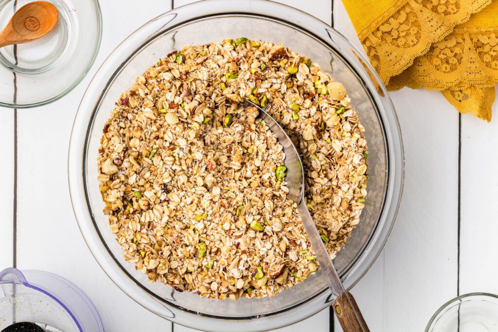 Combining the chopped nuts, seeds, oats, and half the coconut in a large bowl.