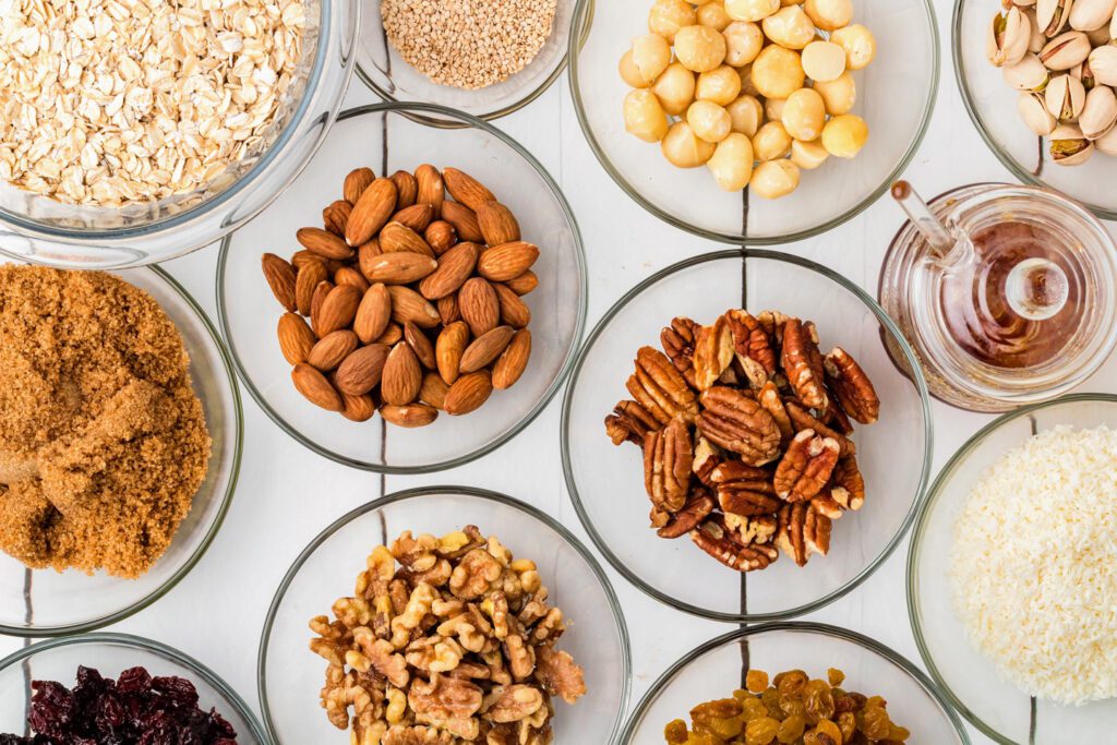 Various nuts, oats, seeds, dried fruits, and shredded coconut in small glass bowls.