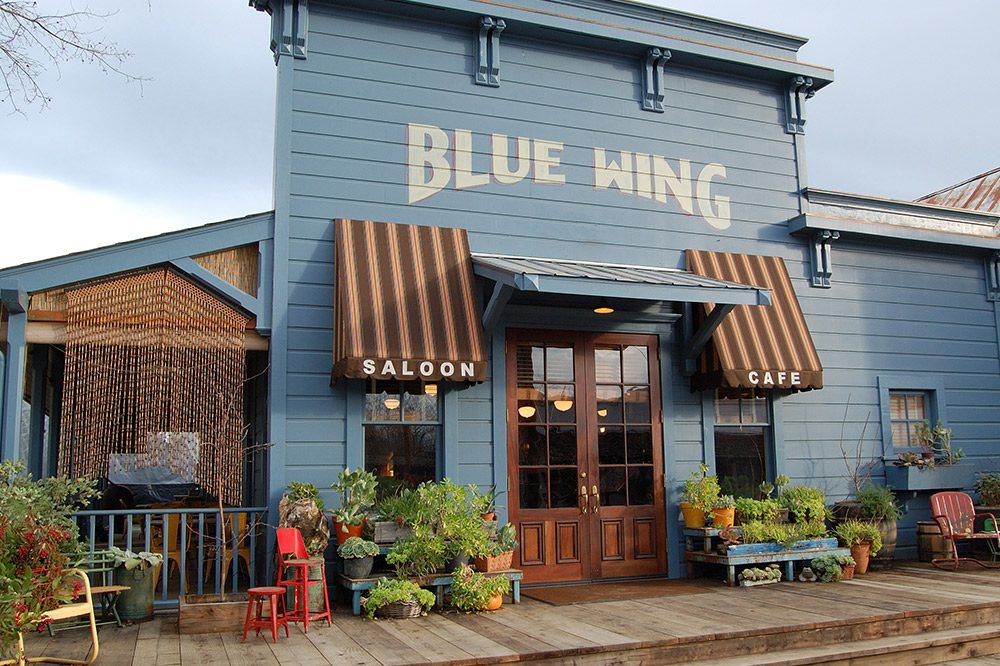 Exterior of a blue saloon and restaurant with striped awnings and a wooden porch