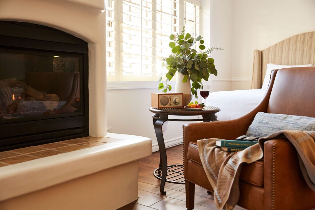 Detail of a guest room with a fireplace, leather chair, cozy blanket, and a Tivoli Bluetooth speaker on a side table.
