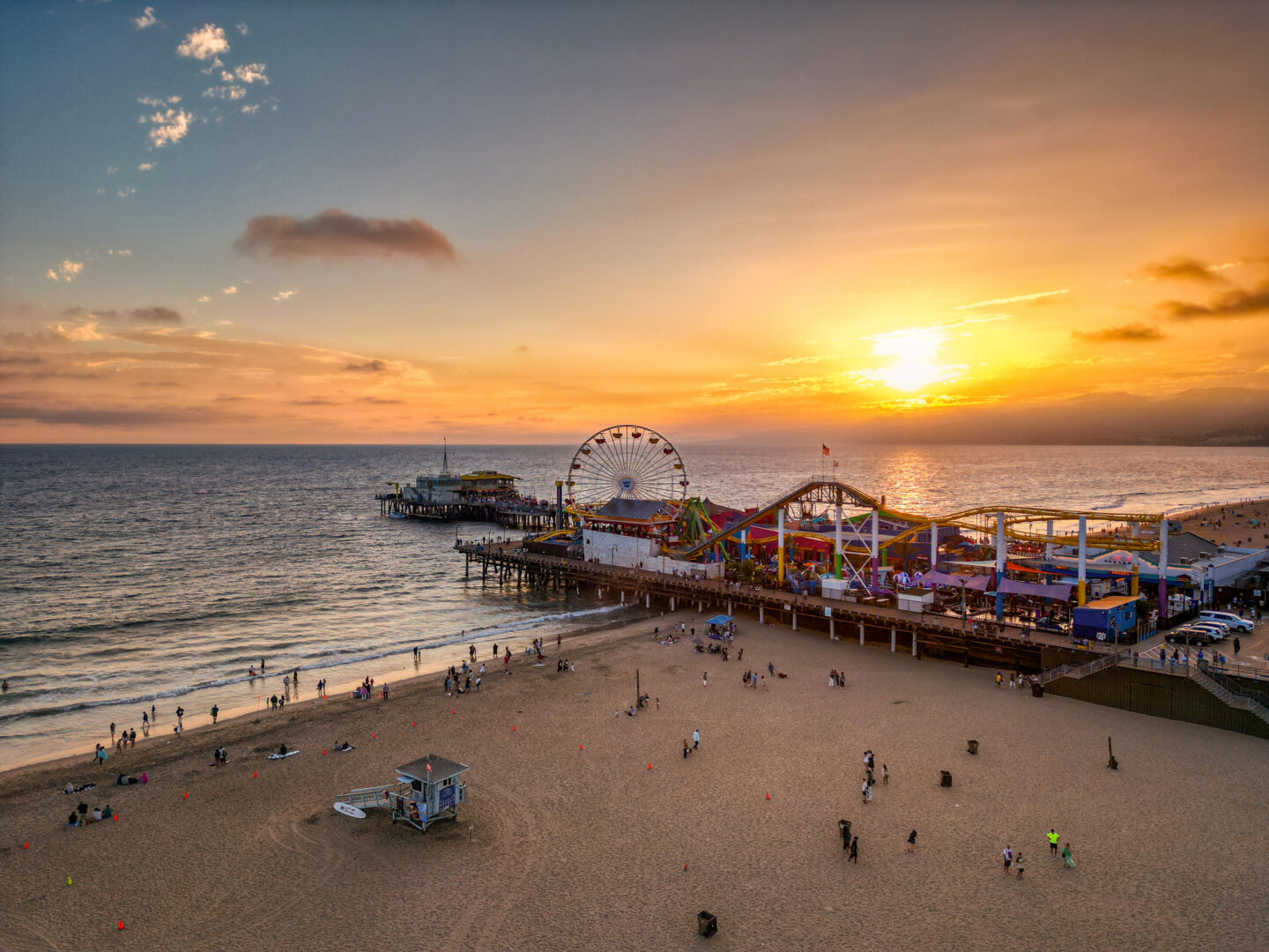 Summer sunset of Santa Monica, California with golden hour lighting and the beach in the foreground. Beach goers enjoy the last bits of sunshine on the beach