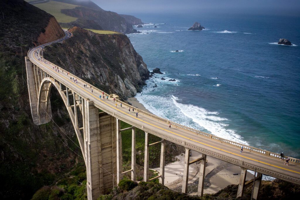 Runners crossing Bixby Bridge in Big Sur with rugged coastline and ocean in the background