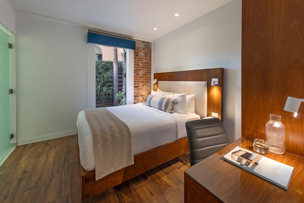 Guest room at Riviera Beach House with a modern bed, desk, a brick accent wall, and door opening to a private patio
