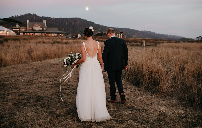bride and groom walking along a grassy coastal bluff