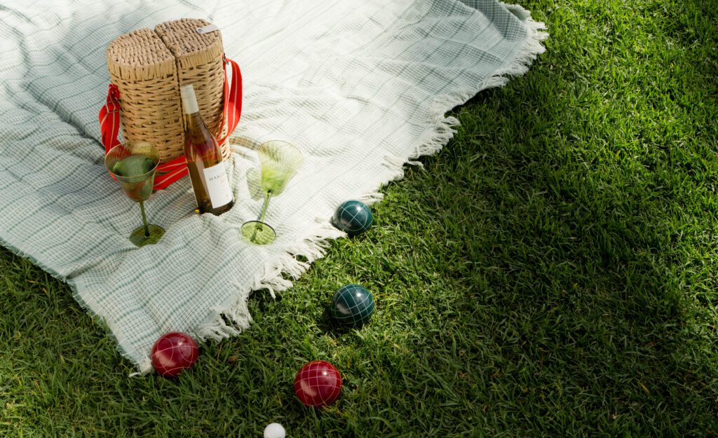 A wine picnic with a blanket and bocce balls on a grass lawn