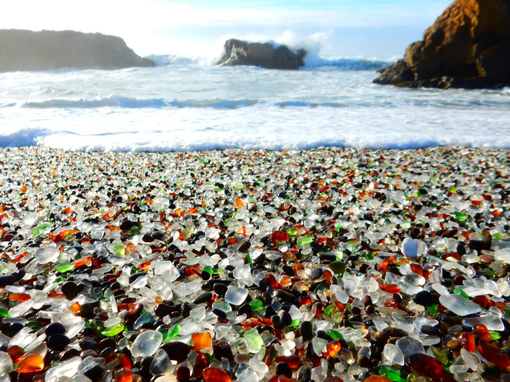 Colorful glass pebbles on a beach with ocean waves and sea stacks in the background