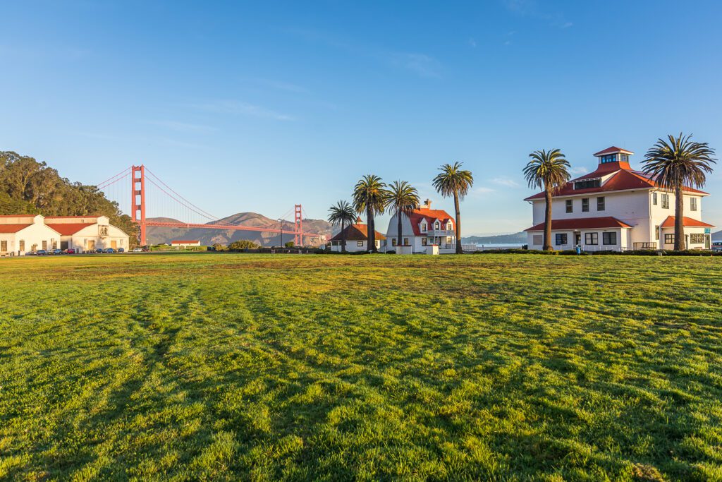 Wide grassy field with historic Presidio buildings and Golden Gate Bridge in the background