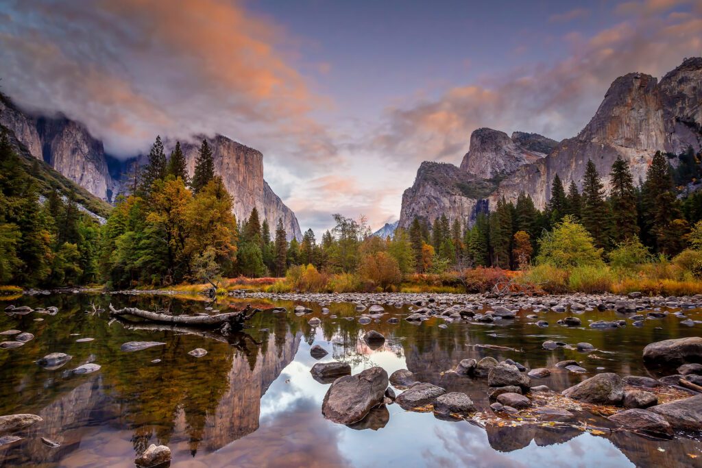 Sunset in Yosemite Valley with a rock-strewn creek in the foreground and towering granite cliffs in the background