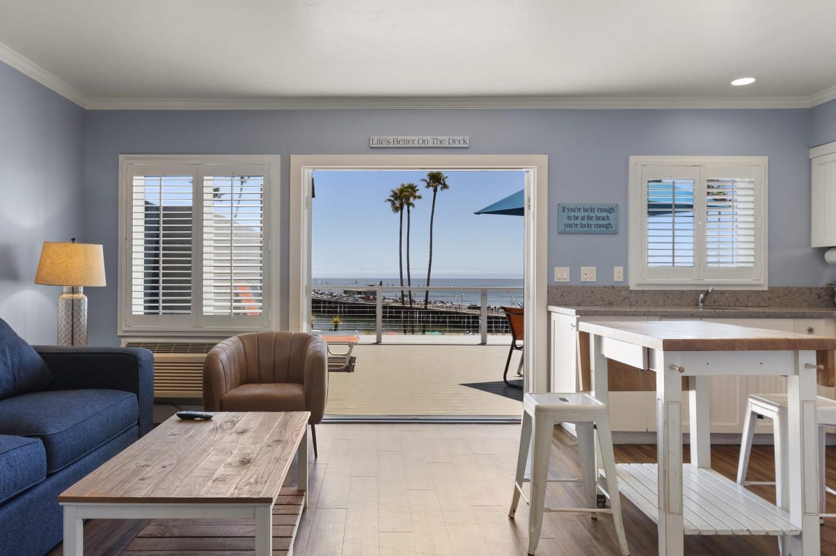 a contemporary living room and kitchen opening to a sundeck with views of the ocean and wharf