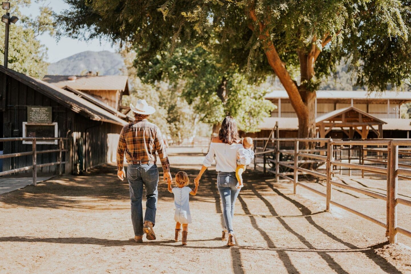 Parents with young kids walking along the horse stables and riding ring at a dude ranch