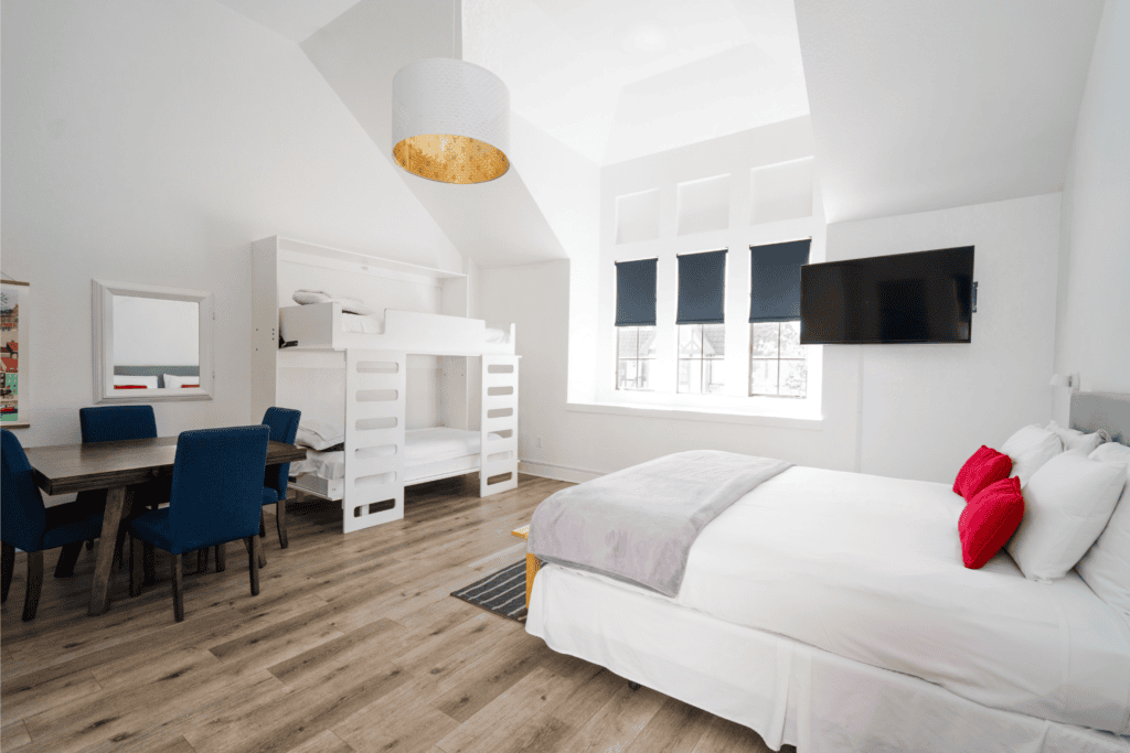 Light-filled modern guest room with king bed, bunk beds, and white and gray color palette with bright red throw pillows