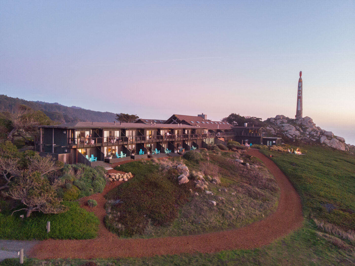 Aerial view of a mid-century modern hotel on ruged coastline with a large sculpture in the background