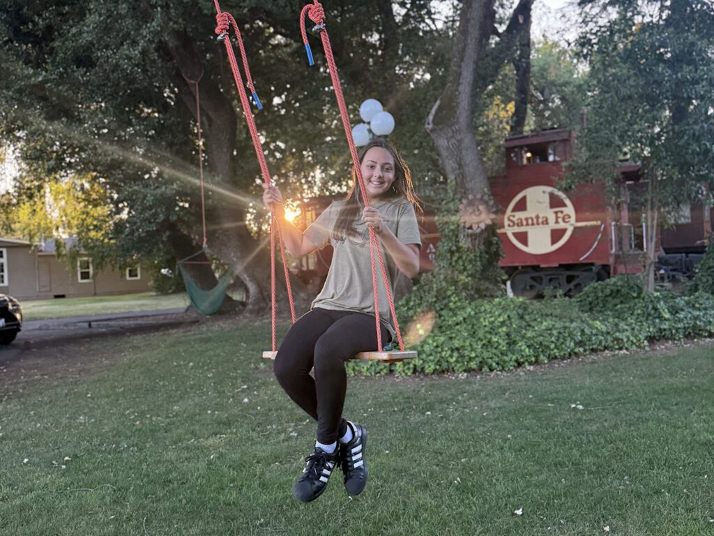 A young girl swinging on a tree swing with a vintage caboose in the background