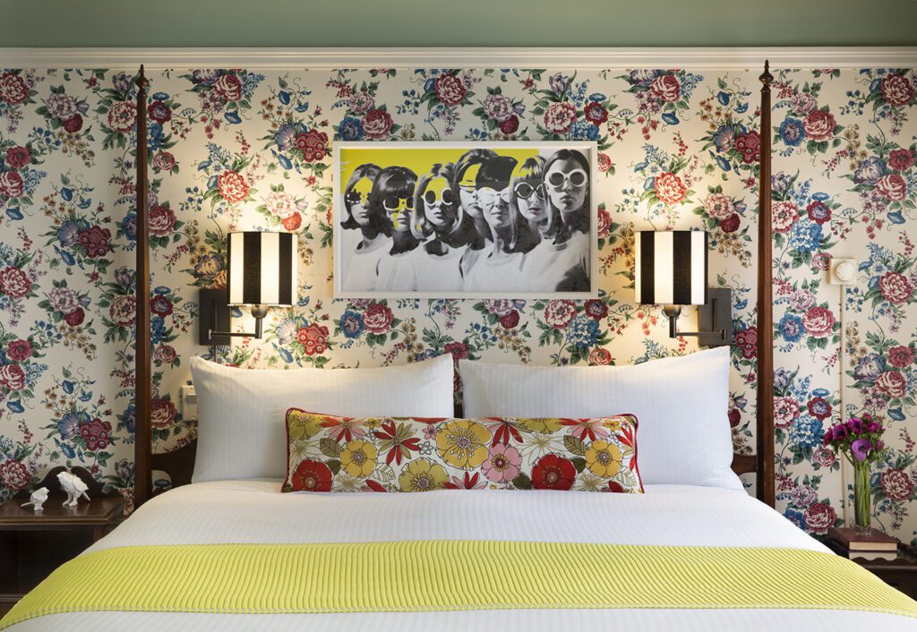 a four poster bed framed with pop art and bold floral wallpaper