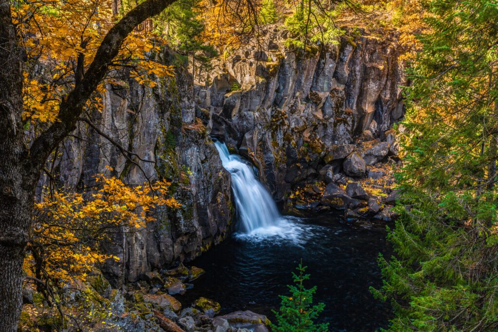 waterfall jutting from a narrow basalt canyon in autumn