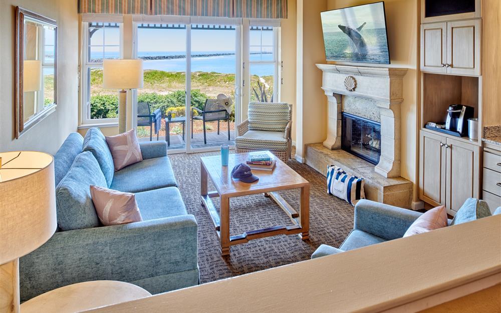 living room of a hotel guest suite with a fireplace and glass door that open to a private patio with ocean views.