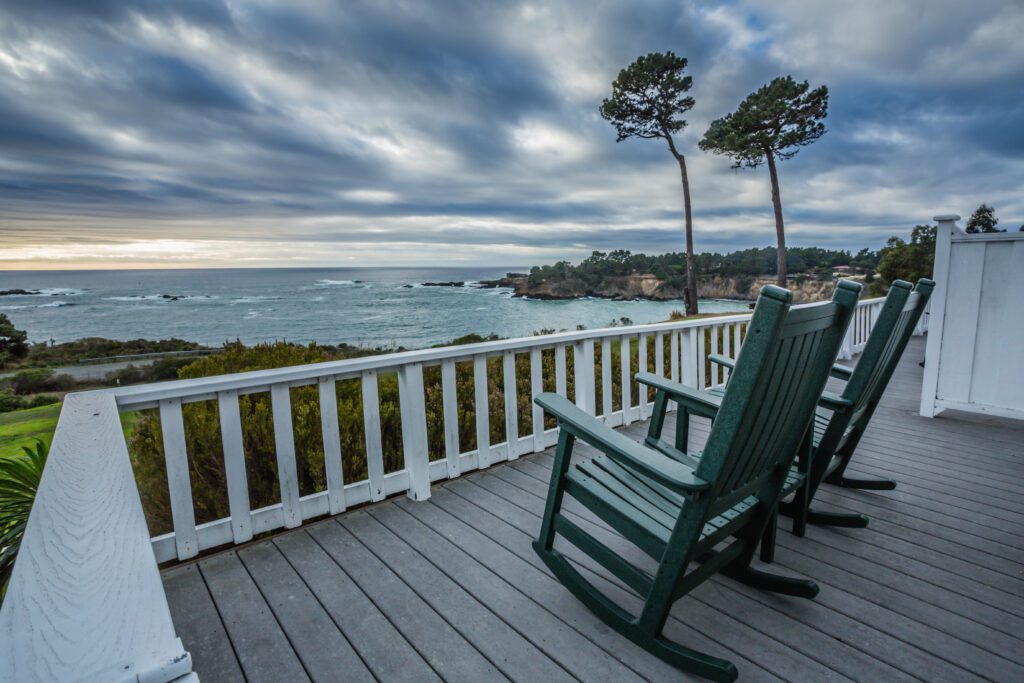 A private deck with hunter green rocking chairs at dusk overlooking the lush grounds and ocean