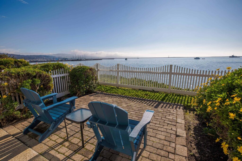 Adirondack chairs on a  brick looking out past a white picket fence to the ocean